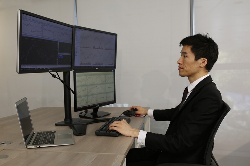 A trader at a desk with three monitors and a laptop (picture taken with Canon EOS 5D Mark III and Canon EF 35mm F2 IS USM)