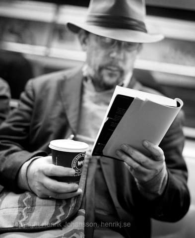 Man is reading book and drinking coffee on the subway (picture taken with Canon EOS 5D Mark II and Canon EF 50mm f/1,4 USM )