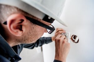 Electrician in glasses is adjusting a wall outlet